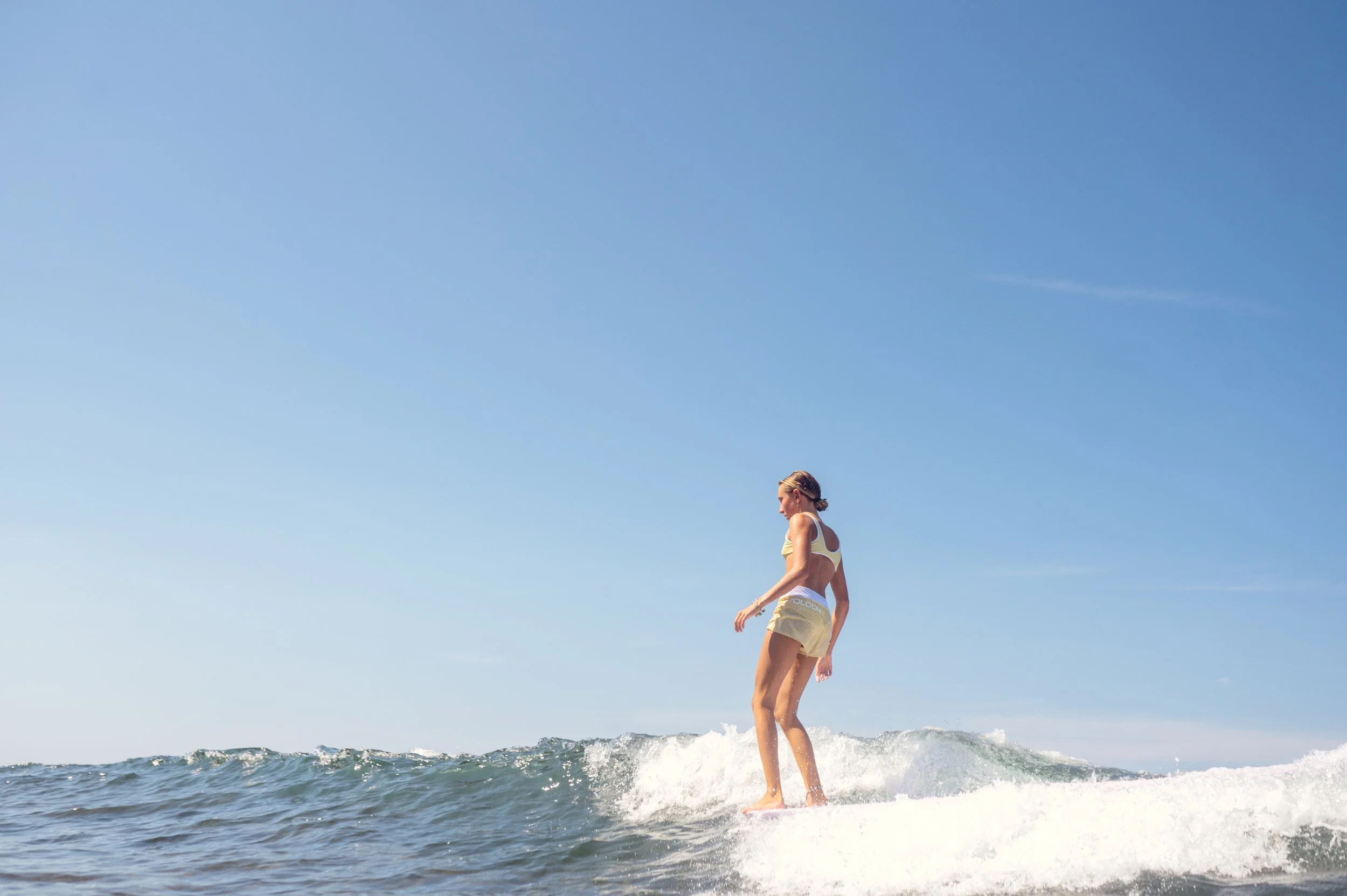 A woman surfing on a wave in the ocean under a clear blue sky.