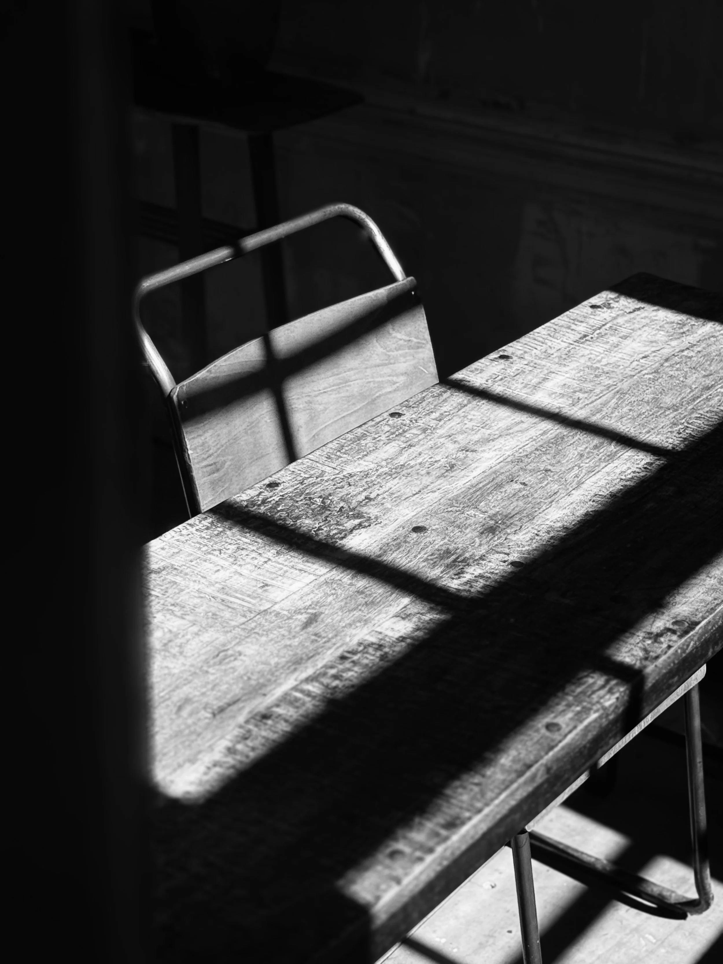 A wooden table and chair in sunlight casting shadows through window bars.