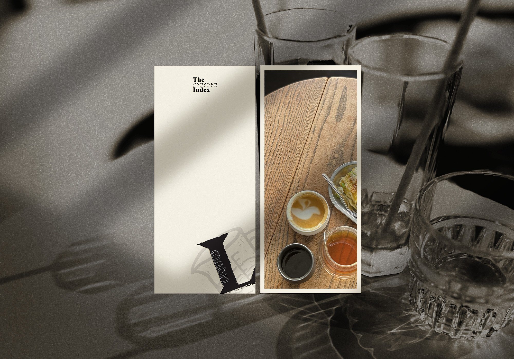 A tabletop with two glasses of water, a paper menu, and a vertical photo showing a wooden table with three small bowls containing various condiments and a dish of salad.