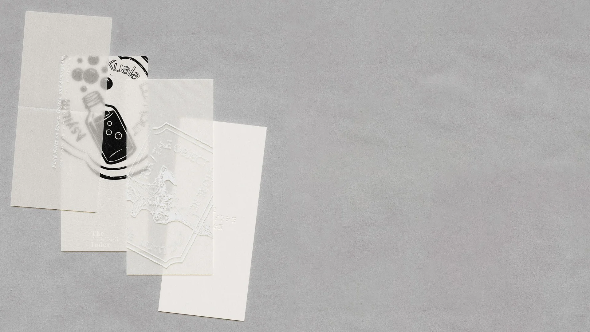 Five overlapping sheets of paper, with various embossed and printed designs, laid out on a gray surface.