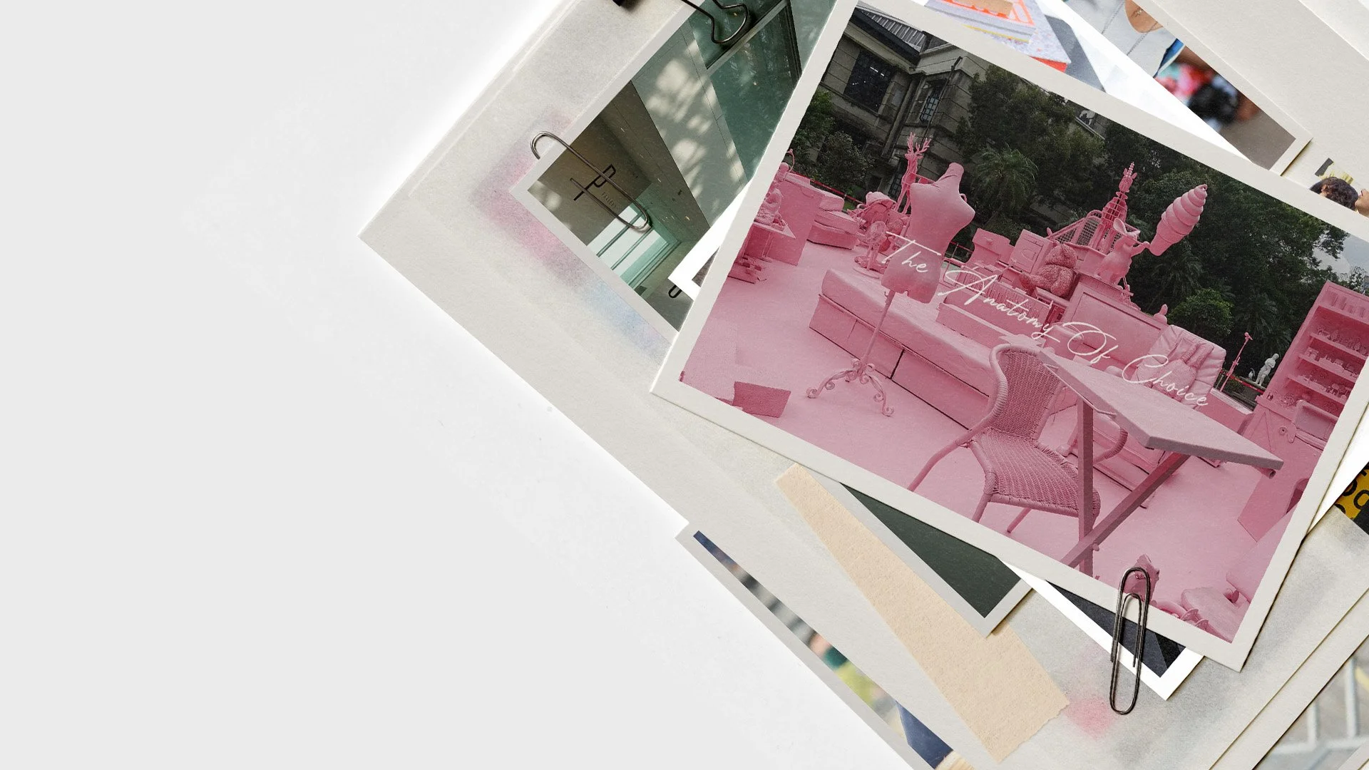 Stack of printed photographs, one featuring a pink outdoor display with mannequins, a pink table, chairs, and various decorative objects, with the text "The Anatomy Of Choice" overlayed.