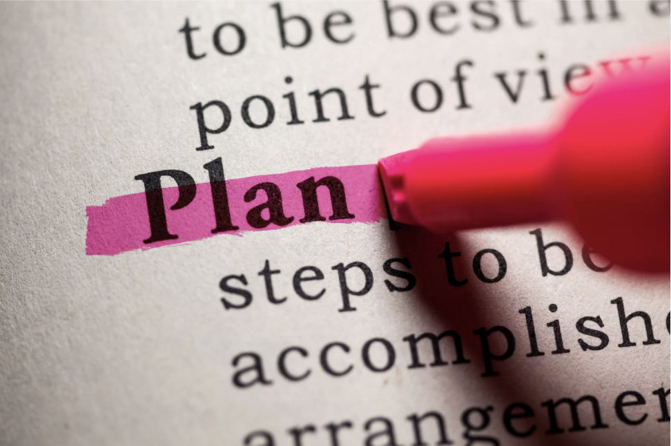 Close-up of a pink highlighter highlighting the word 'Plan' on a page of printed text.