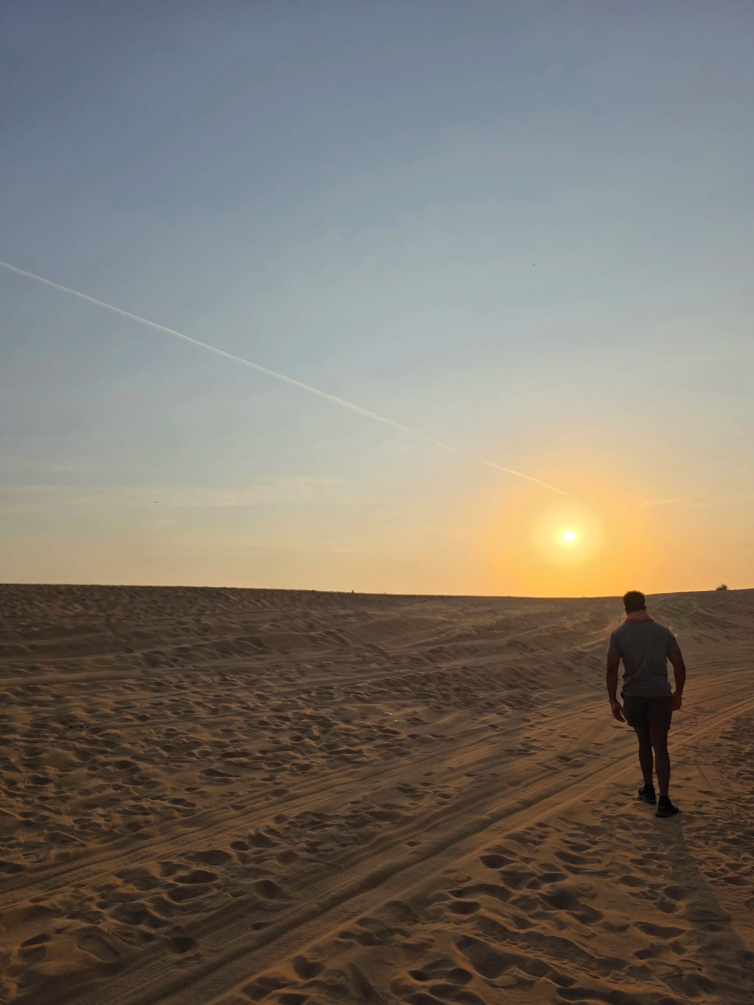 A person walking on sand dunes during sunset in a desert landscape.