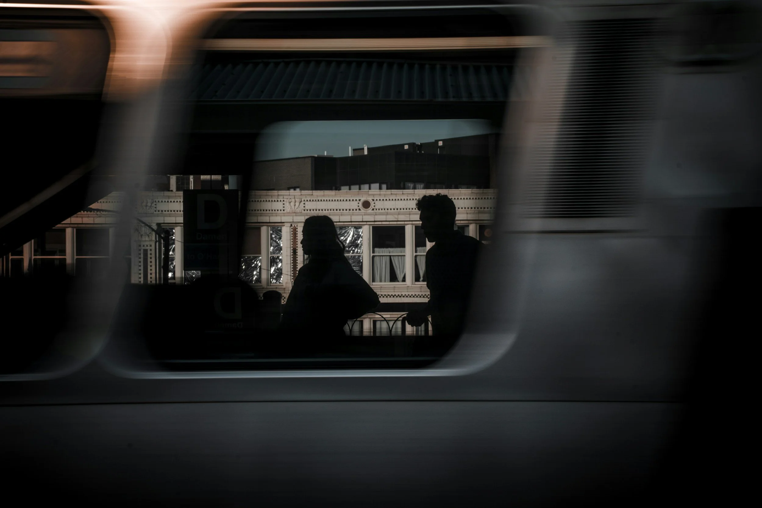 Silhouettes of two people seen through a window reflection on a building across the street