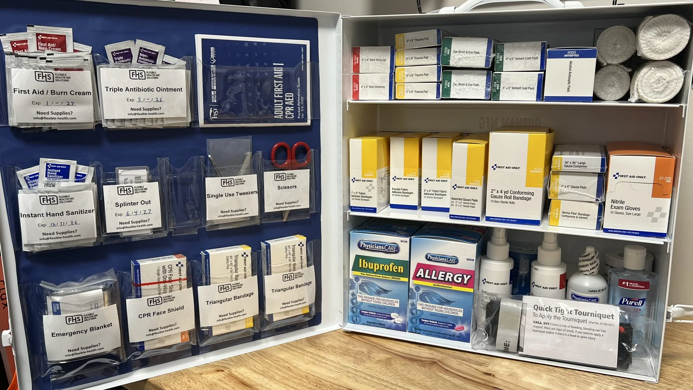 Medical supply station with various first aid supplies including bandages, antiseptic ointments, gloves, scissors, tape, and medications on shelves and hooks.