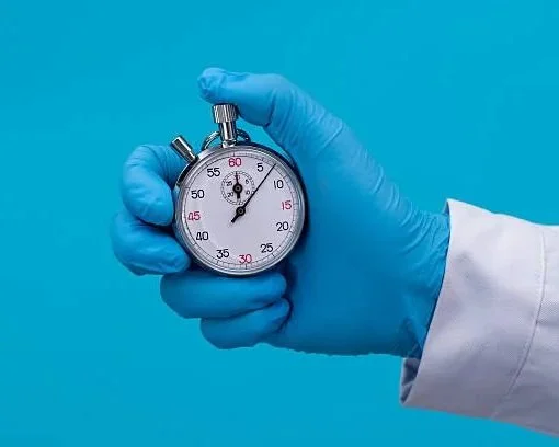 Hand wearing a blue glove holding a silver stopwatch against a blue background.
