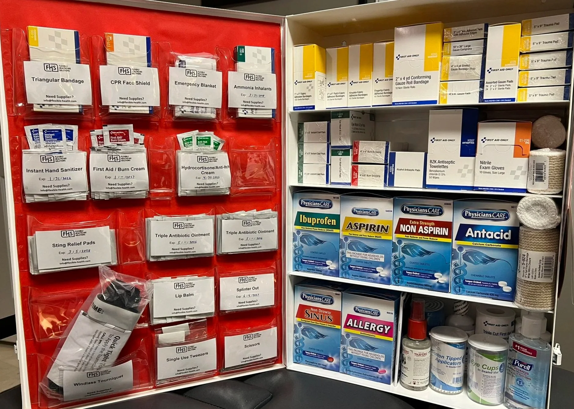 Medical supplies on a red display with various first aid items, including bandages, CPR face shields, emergency blankets, aspirin, allergy medication, eye cups, and other first aid products in packaging.