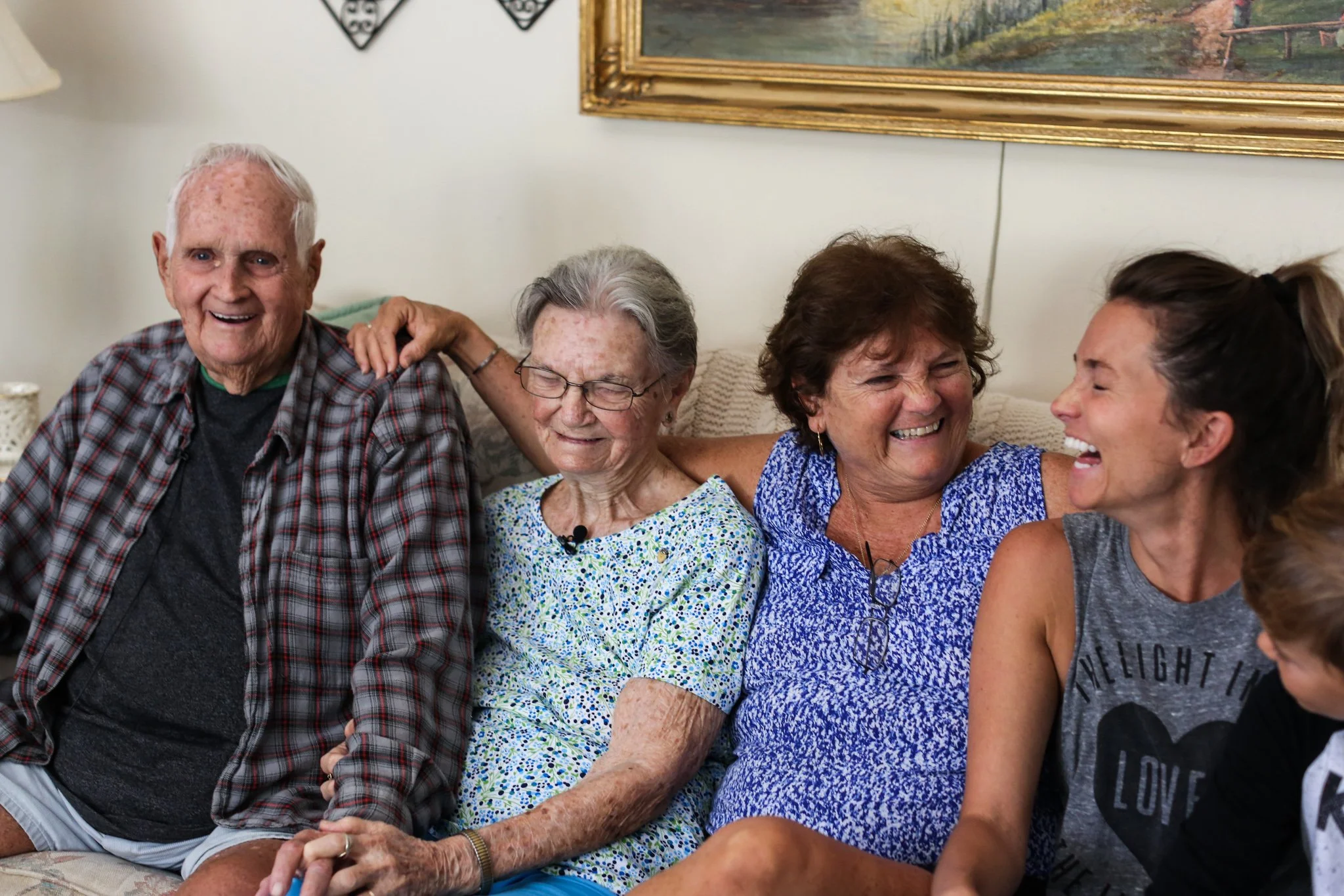 Four generations of a family spending time together and laughing on a couch in their living room.
