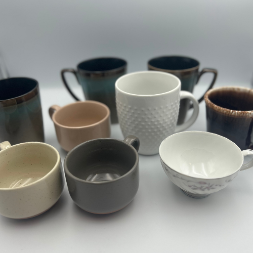 Collection of various ceramic mugs and cups in different colors and designs on a white surface.