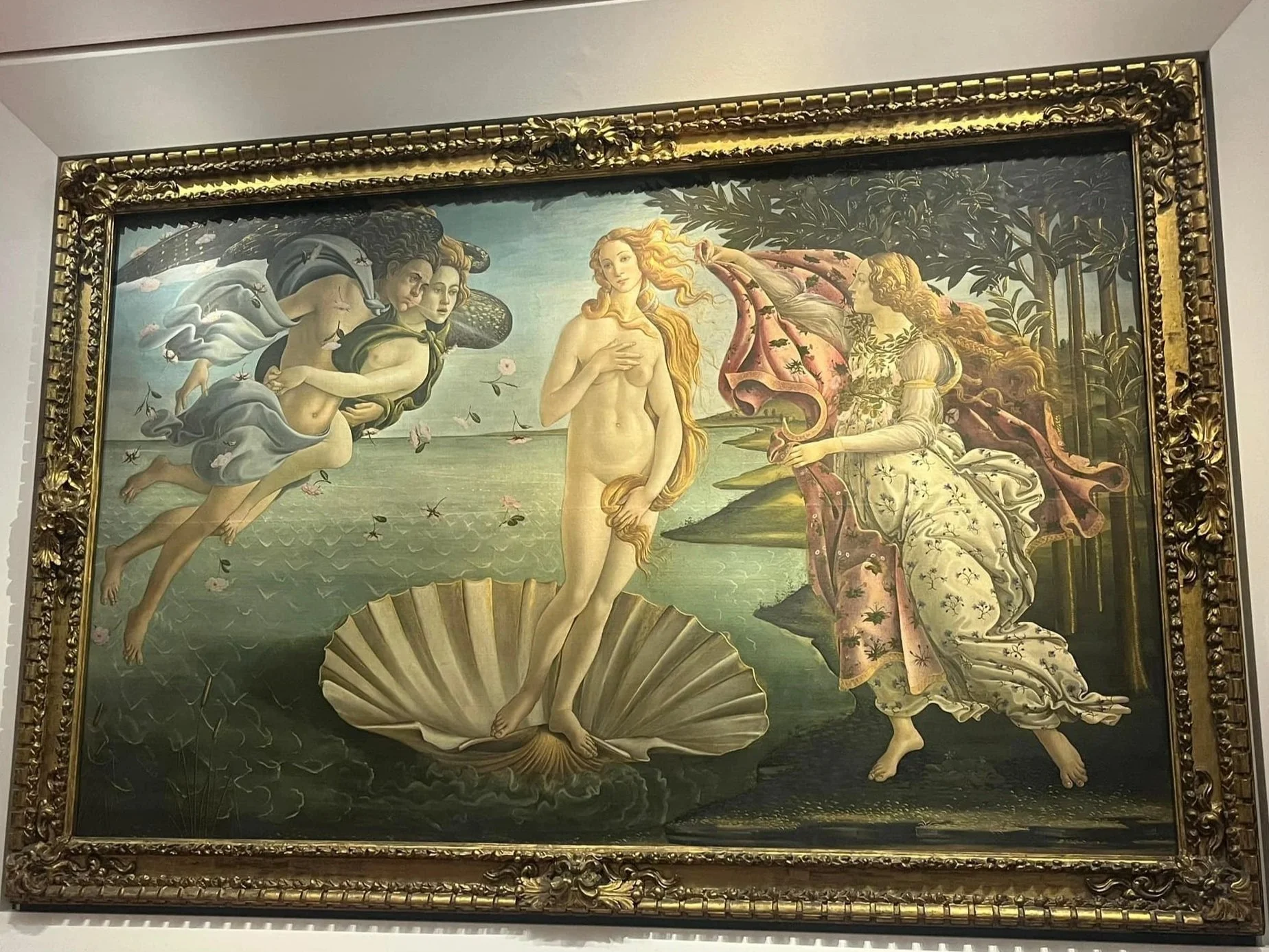 A famous painting depicting the mythological scene of the birth of Venus, showing Venus emerging from a seashell, with three figures, including one holding a drapery, in a natural setting with trees and a body of water.