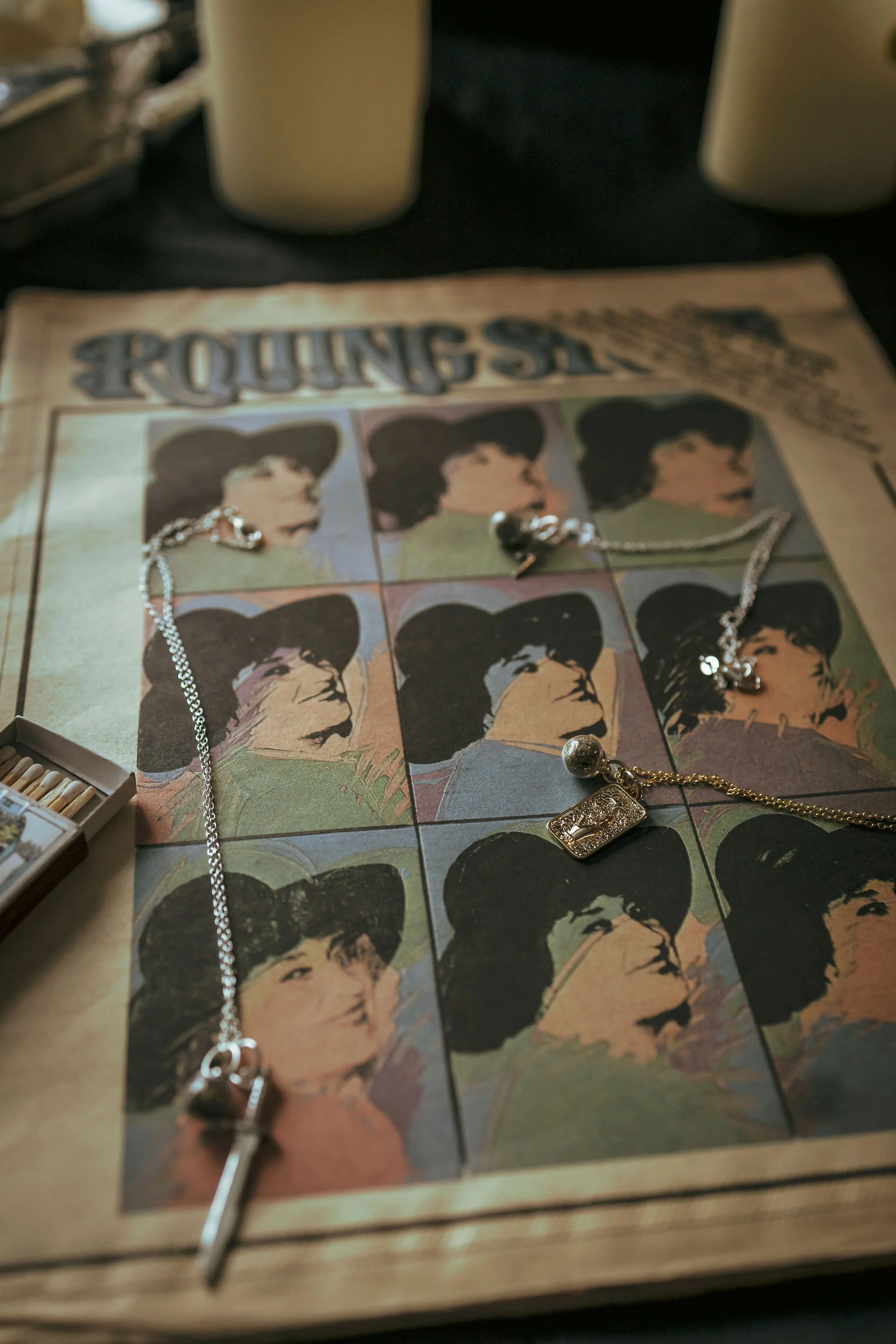 Jewelry, including a silver necklace, a gold chain with a pendant, and earrings, placed on a vintage Rolling Stone magazine featuring images of The Rolling Stones band members.