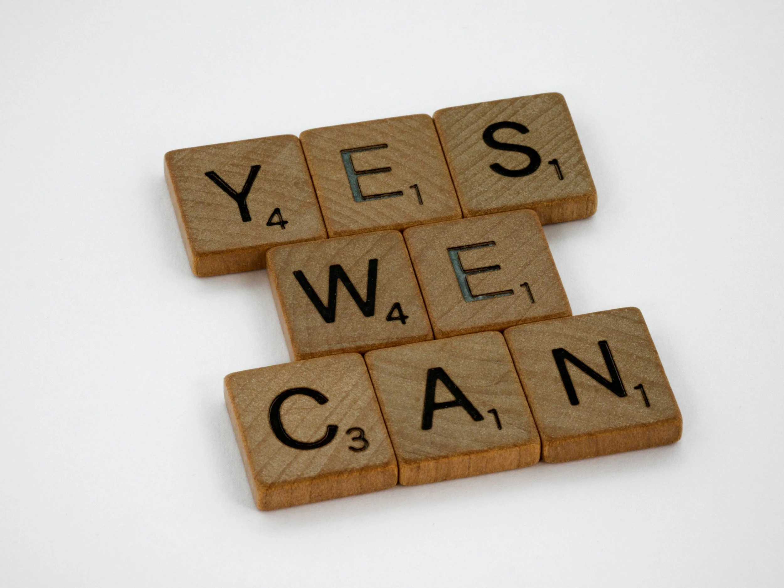 Wooden Scrabble tiles spelling out "YES WE CAN" on a white background.