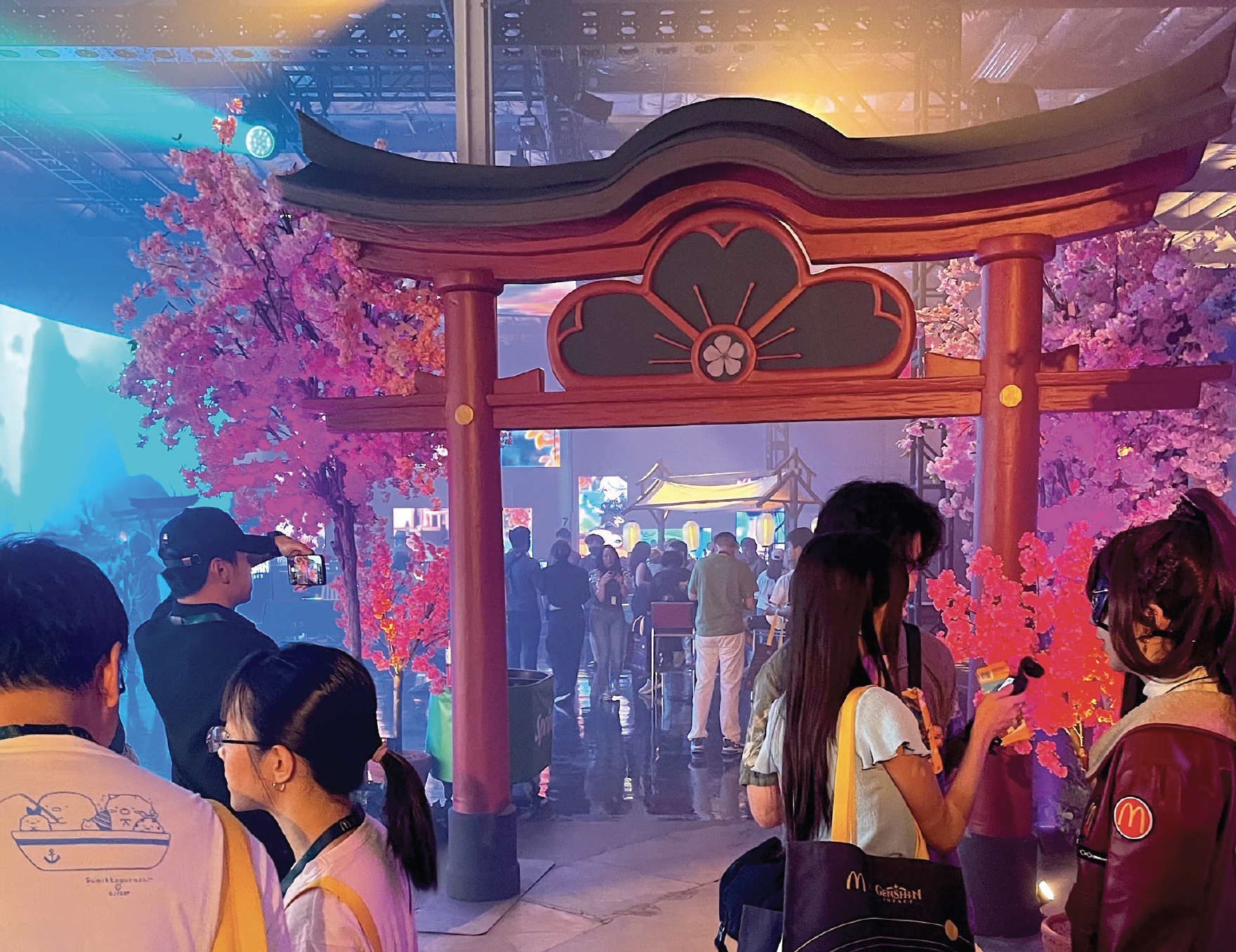 People gathered at an indoor event with pink cherry blossom trees, a large red torii gate, and traditional Asian decorations.
