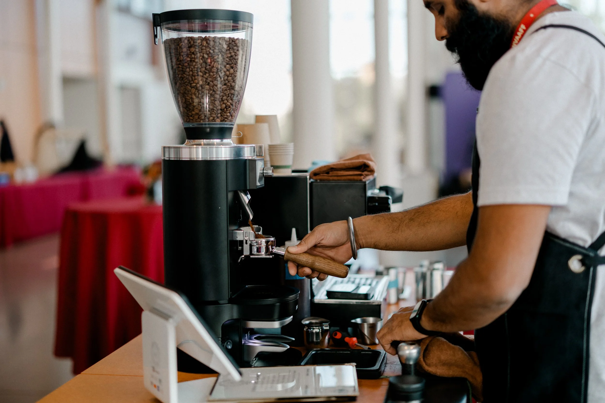 Barista preparing espresso at coffee shop counter. Coffee grinder filled with beans and espresso machine visible.