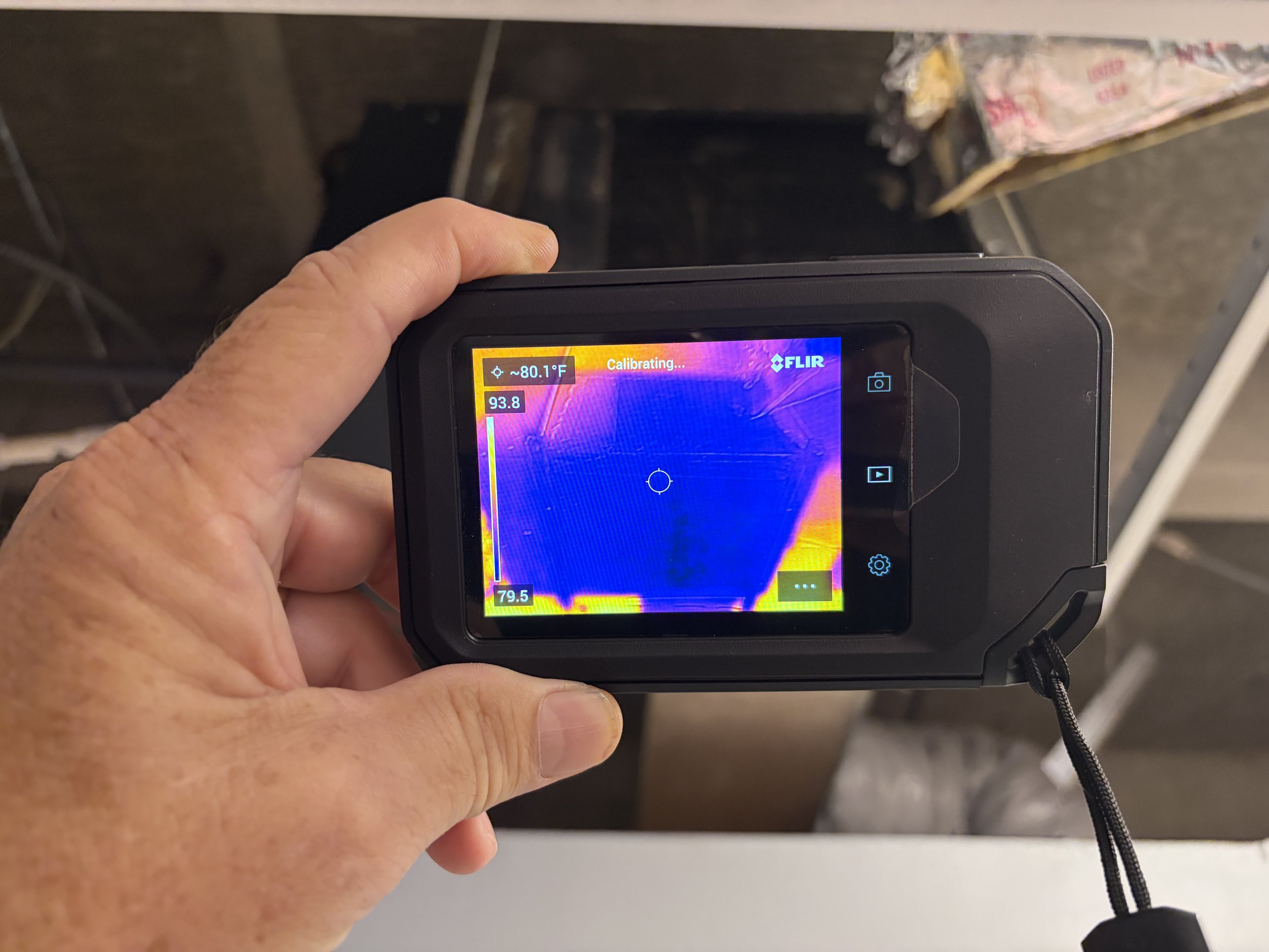 A person holding a thermal imaging camera showing a temperature readout of around 80.1°F and a colorful thermal image.