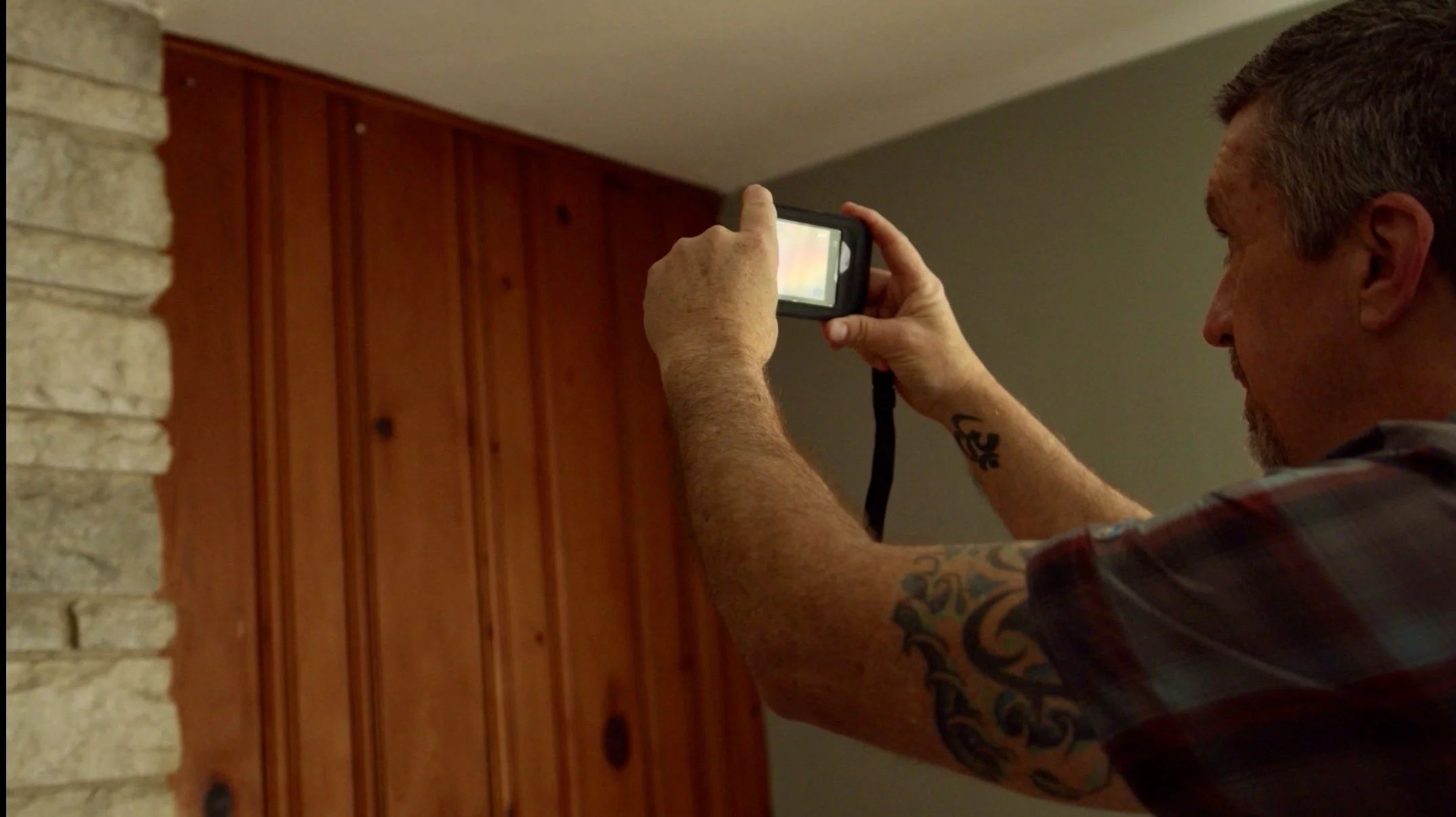 A man taking a thermal image in a room with wooden paneling on the wall.