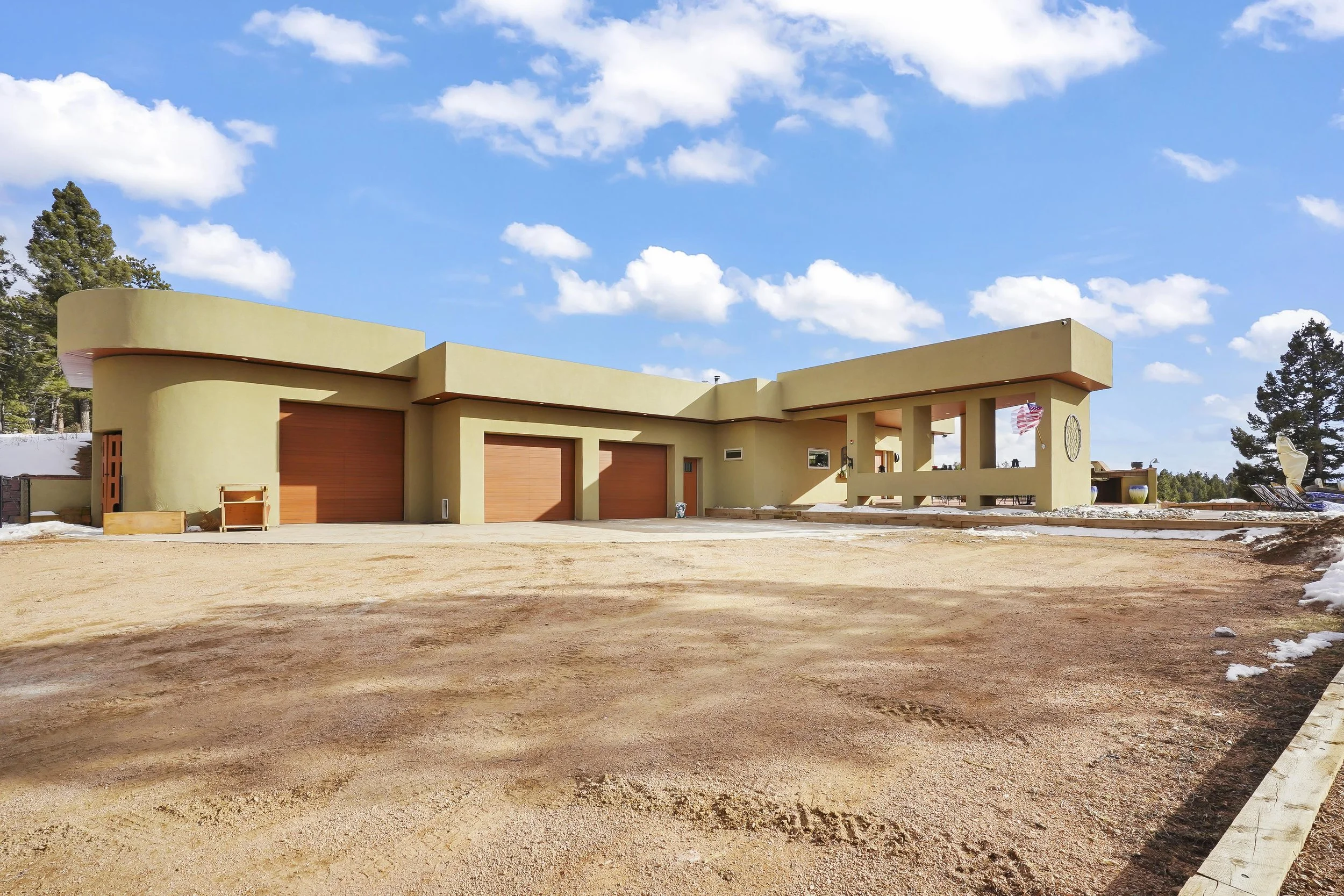 Modern house with yellow exterior, three garage doors, a covered porch area, and flagpoles with flags, under a blue sky with clouds.
