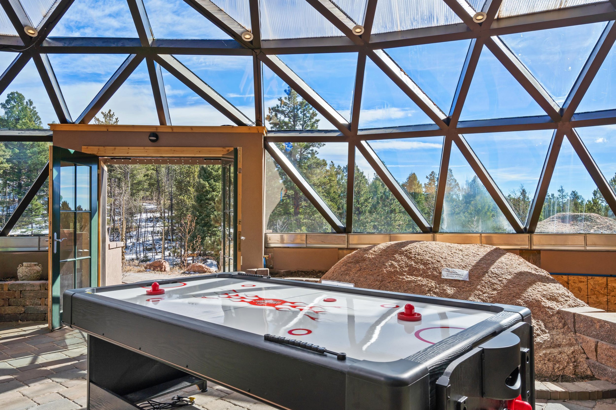 Indoor ice hockey table near large glass windows showing a scenic outdoor landscape with trees and snow.