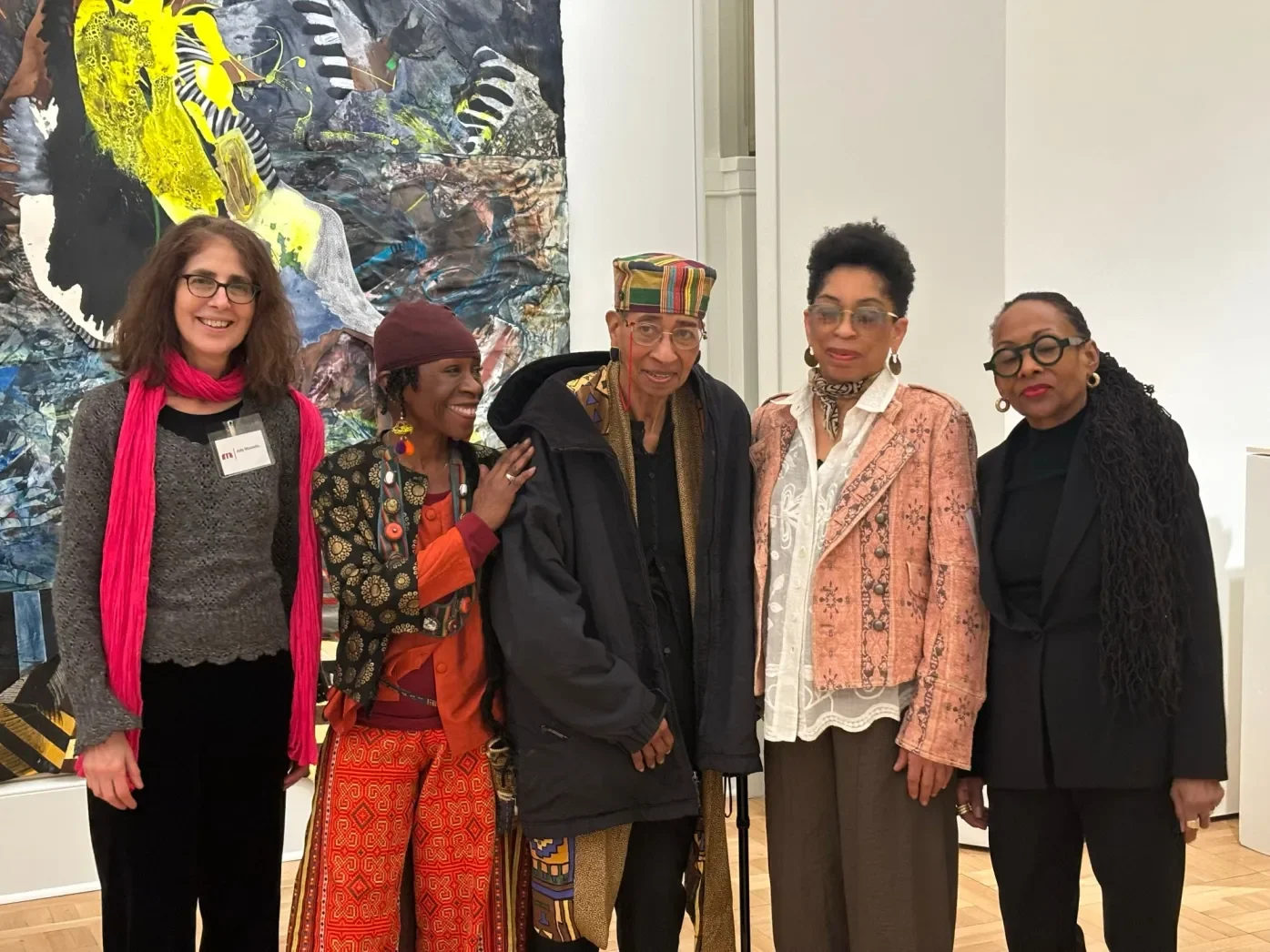Five women standing together in front of an abstract artwork in an art gallery.