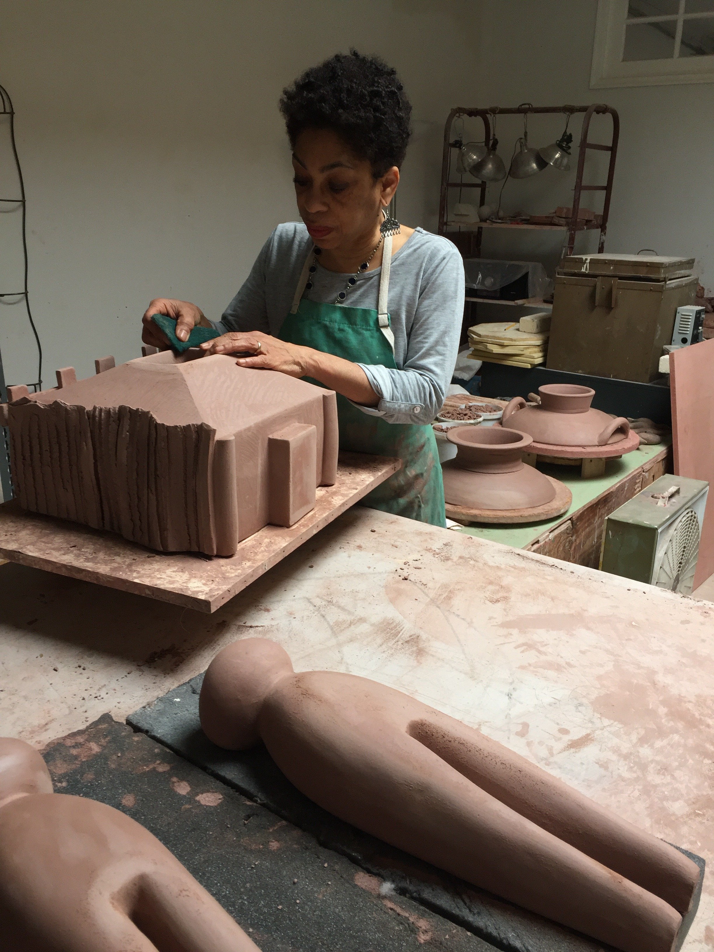 Artist, Syd Carpenter, sculpting clay on a worktable with unfinished pottery and ceramic pieces in the background.