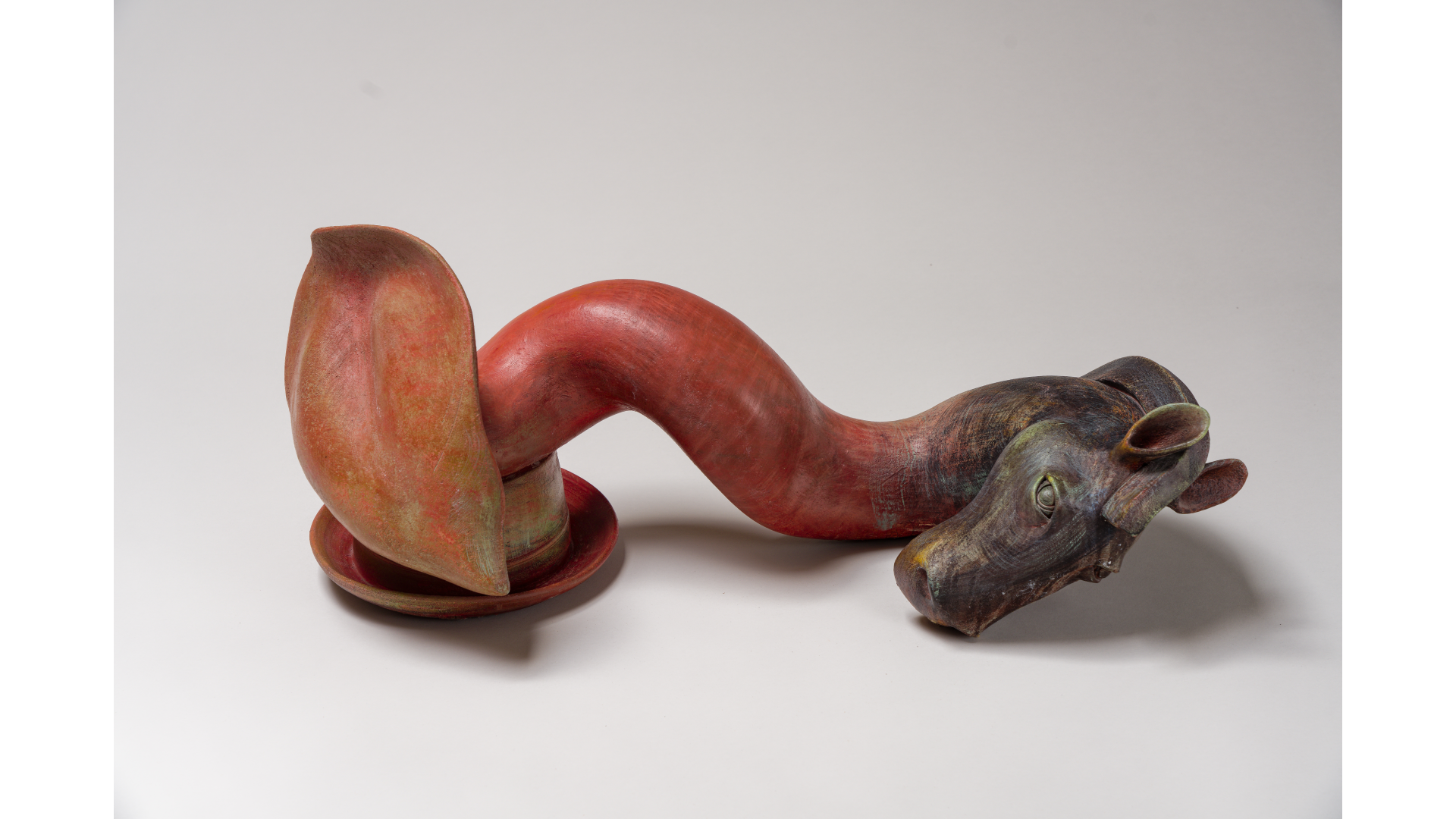 A sculpture made from carved wood, with a red curved body and a detailed head, set against a plain white background.