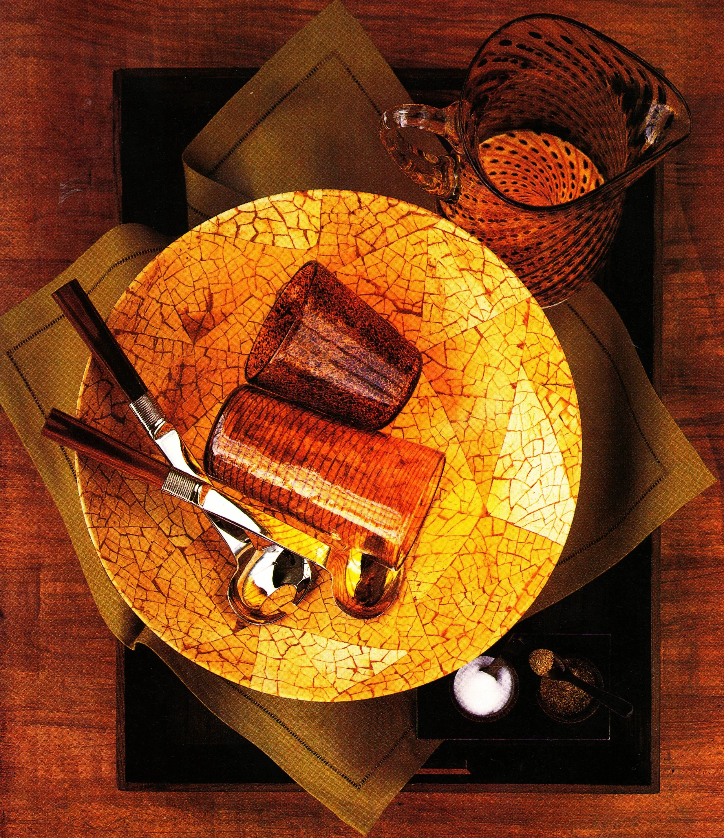 A table setting with a yellow plate, tortoise shell glasses, a tortoiseshell glass pitcher, and utensils, viewed from above.