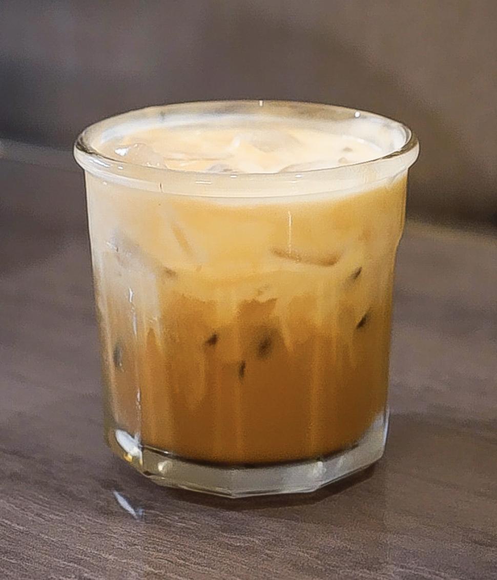 A glass of iced coffee with milk on a wooden surface.