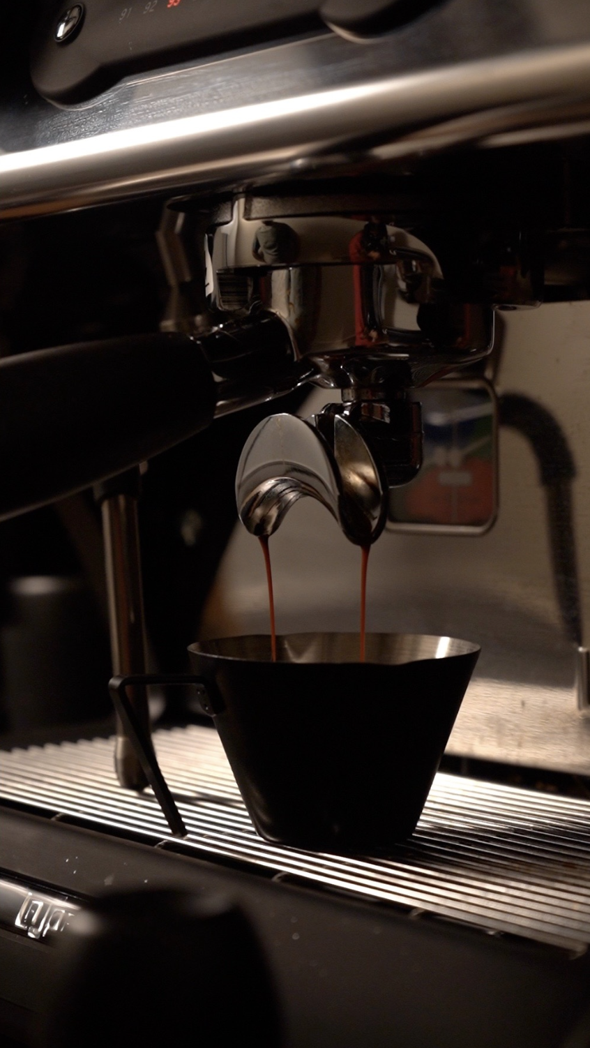 Espresso brewing from a coffee machine into a black cup.