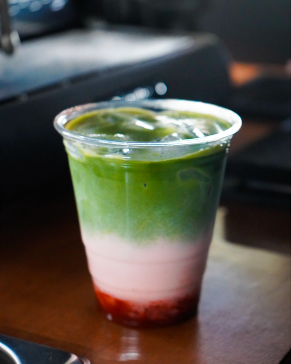 A layered multi-colored drink in a clear plastic cup with a straw, containing a red layer at the bottom, a white middle layer, and a green top layer.