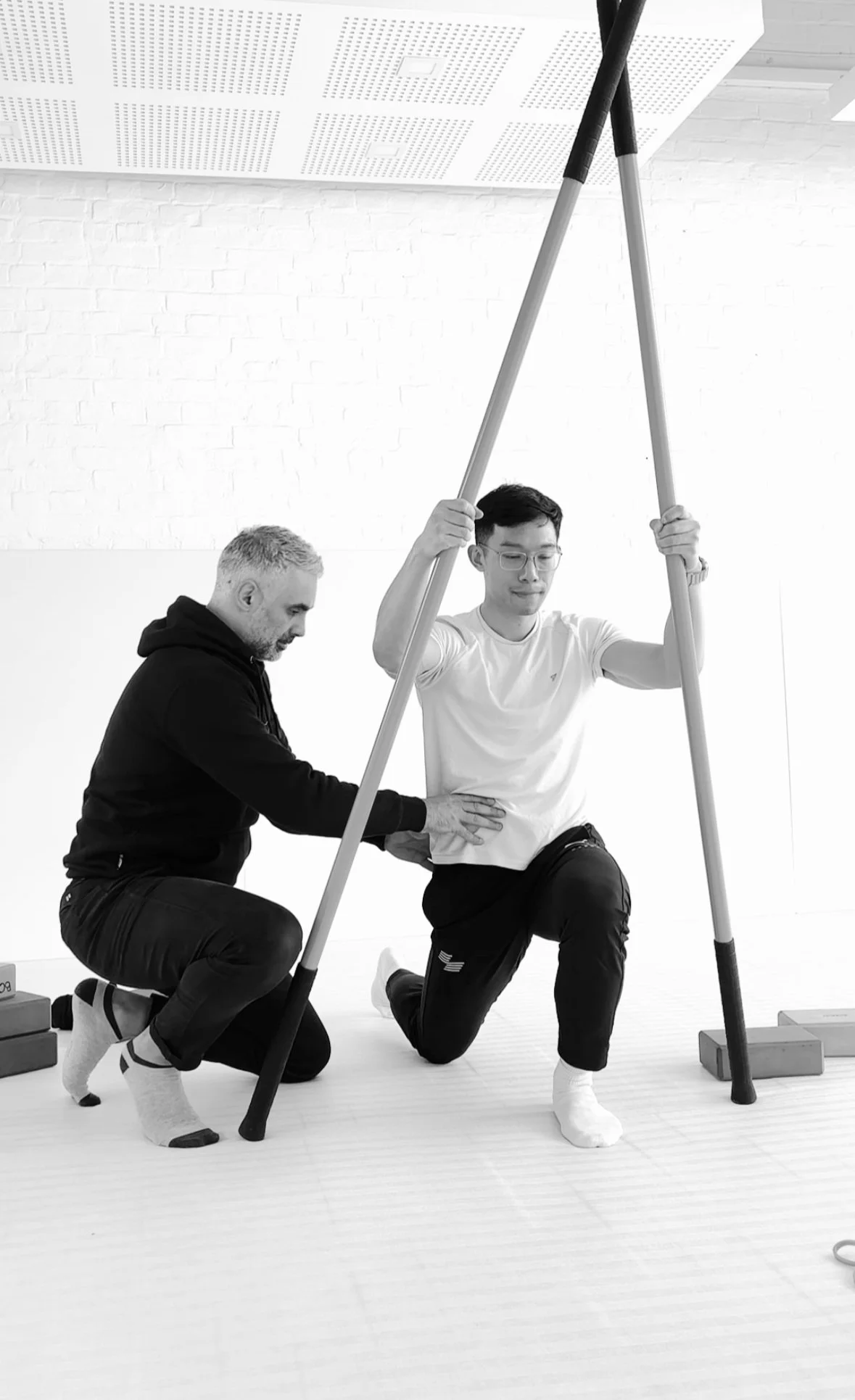 A person practicing a lunge exercise under the supervision of a trainer in a gym or fitness studio.