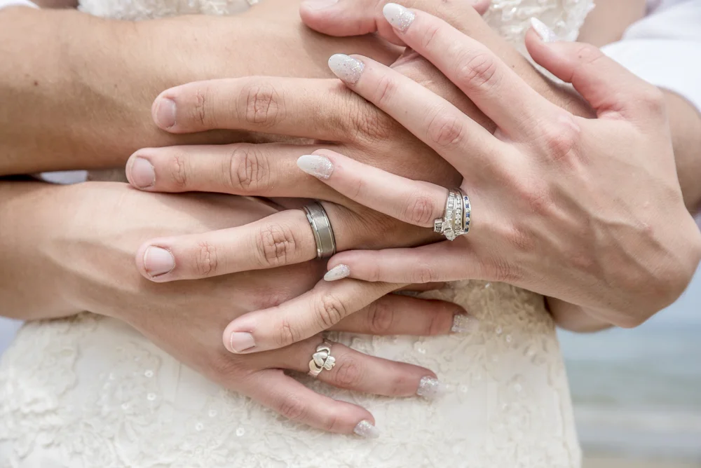 Close-up of hands with wedding rings, embracing a person's waist in a wedding dress.