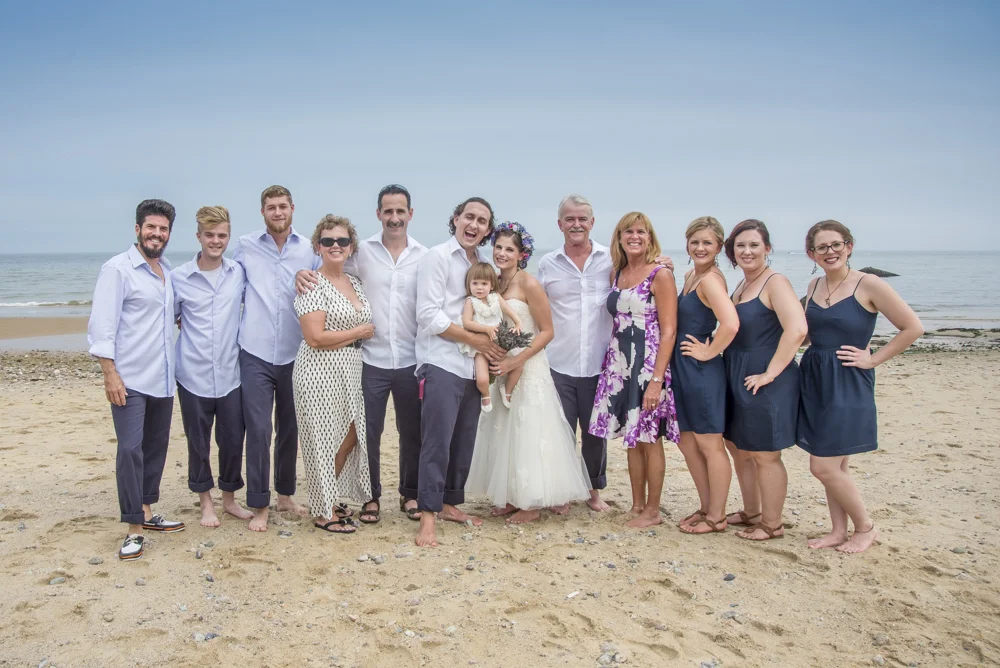 Group of people in wedding attire on the beach, celebrating and smiling.