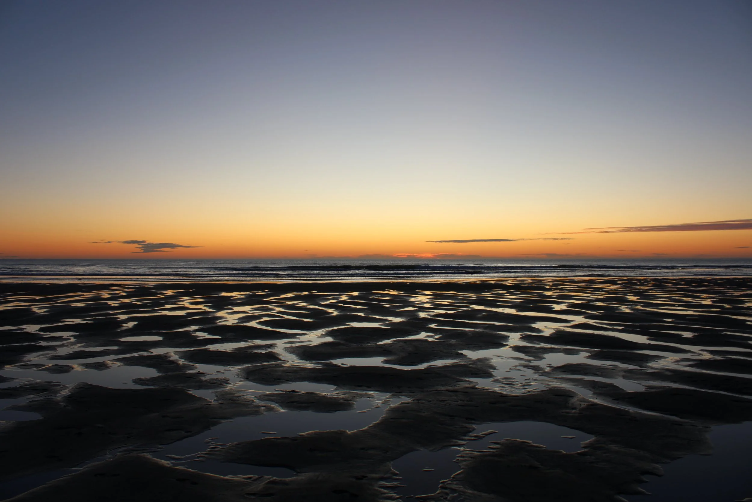 Sunset over a beach with tide pools and wet sand.