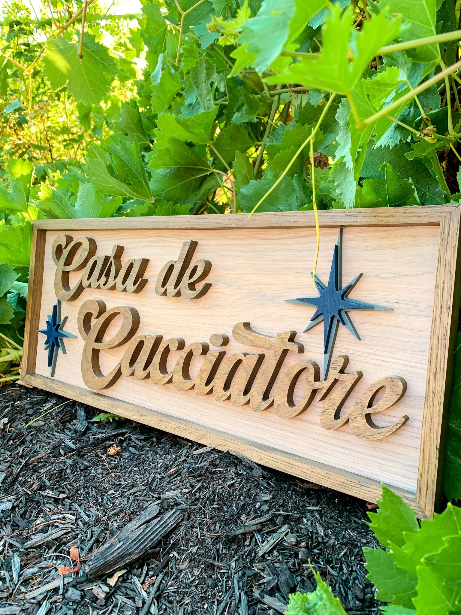 A decorative wooden sign is placed on the ground among mulch and green leaves.