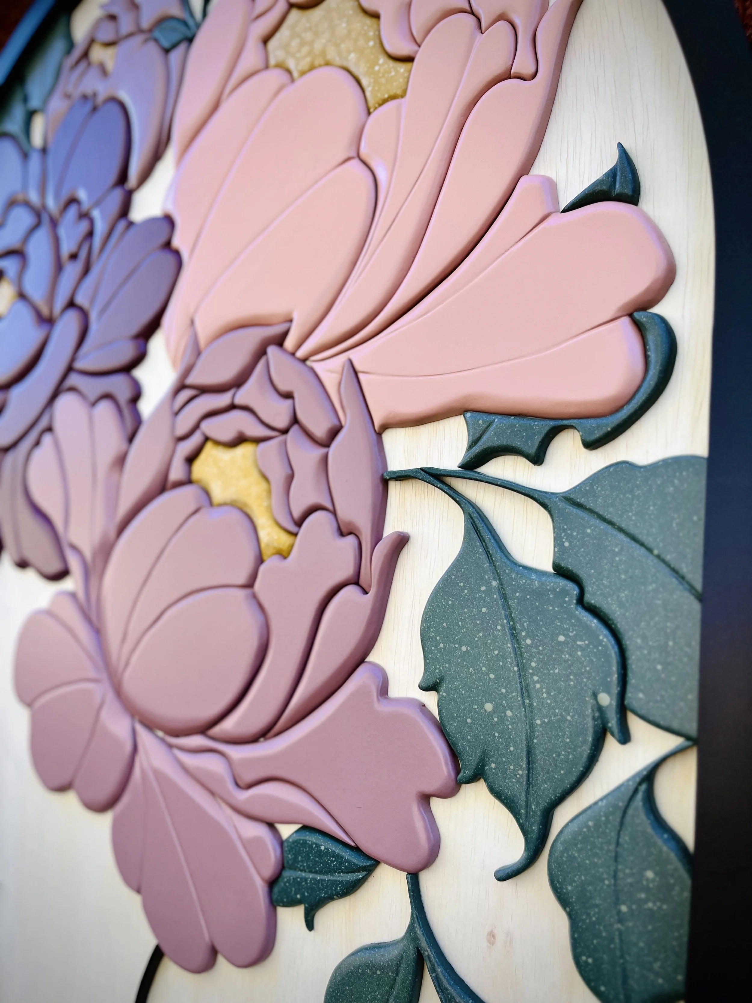 Close-up of a colorful floral artwork with pink and purple petals and green leaves, made of layered materials resembling foam or painted wood.