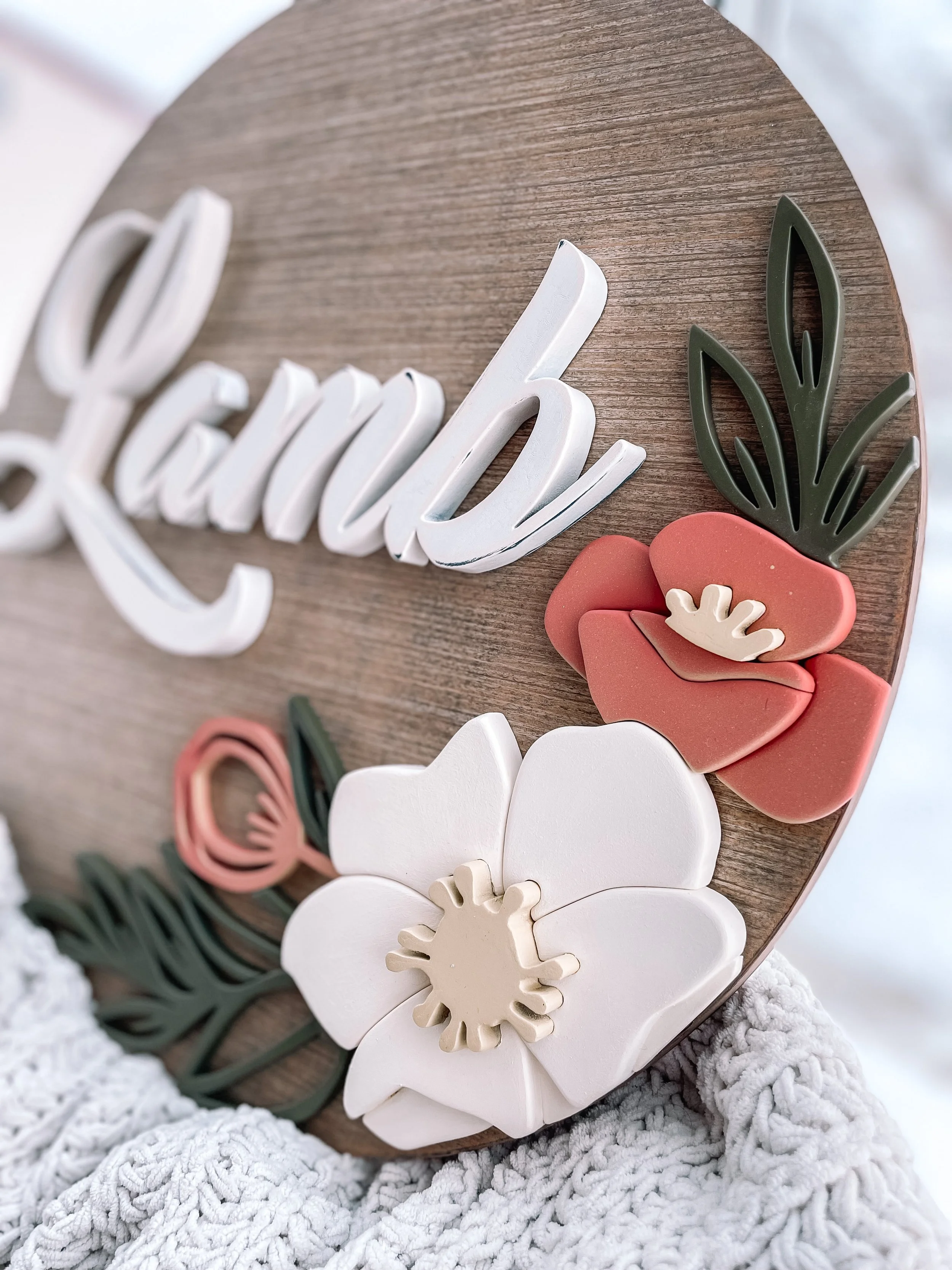 Decorative wooden sign with the word "Lavanda" in white script and 3D flowers and leaves in pink, white, green, and beige.