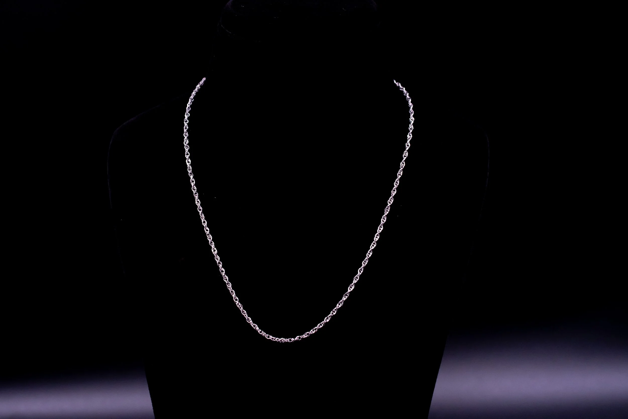 Silver chain necklace displayed on a black mannequin bust against a dark background.