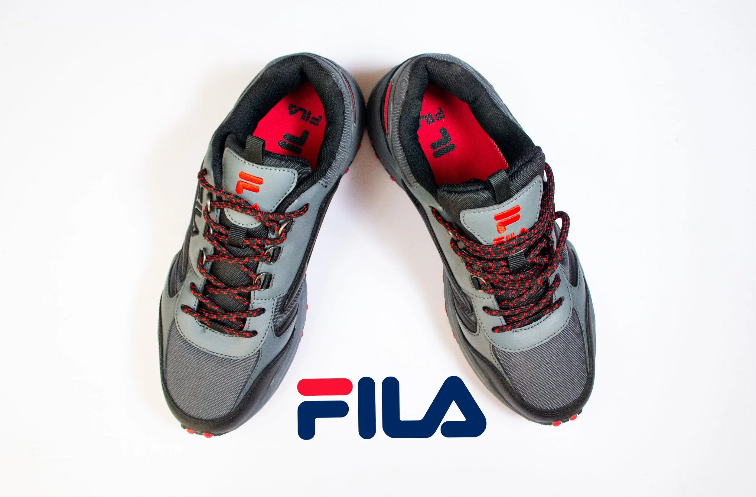 Pair of gray and black FILA athletic shoes with red and black laces positioned above a FILA logo on a white background.
