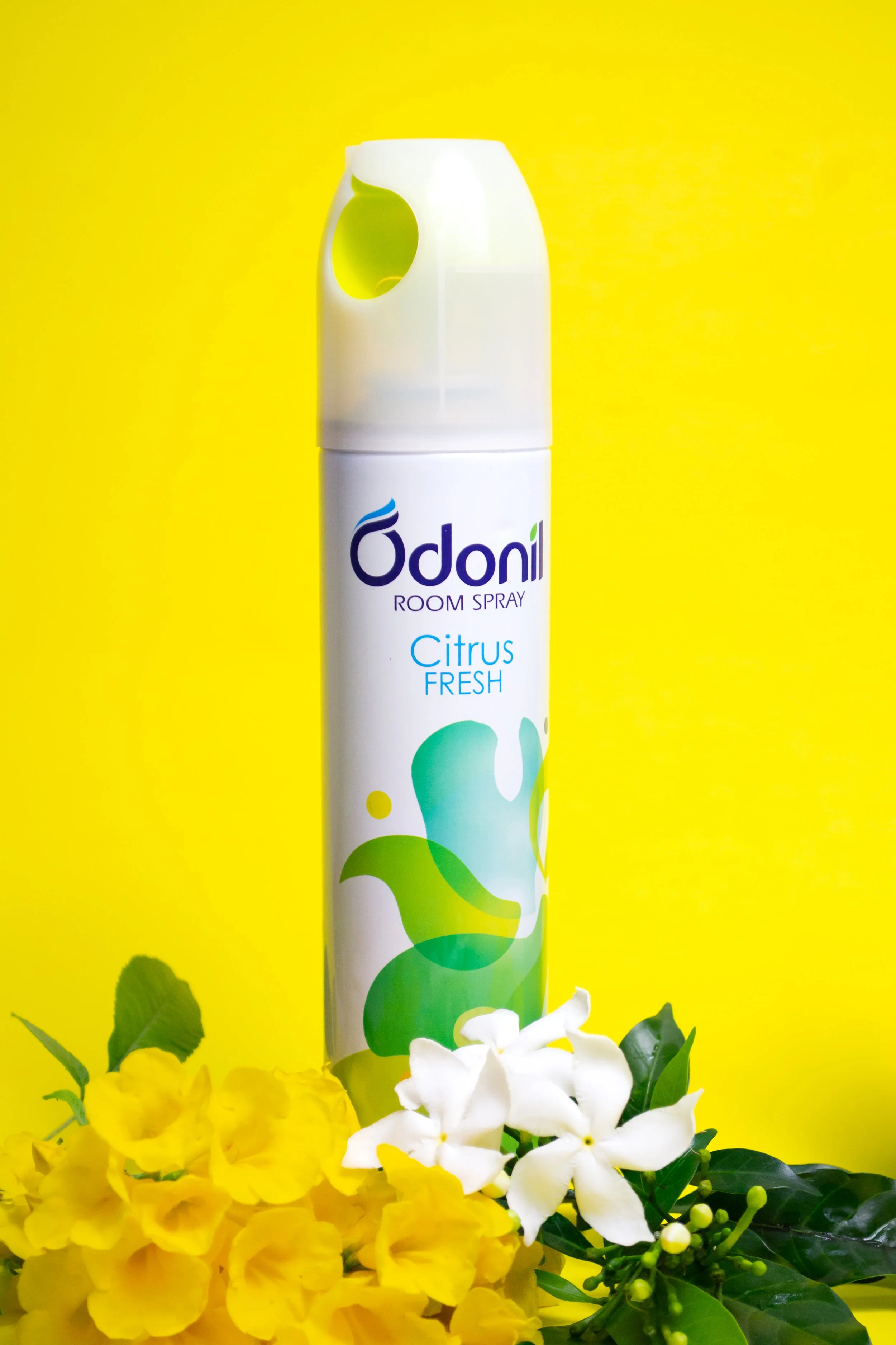 A can of Odani Citrus Fresh room spray with yellow and white flowers in front, set against a yellow background.
