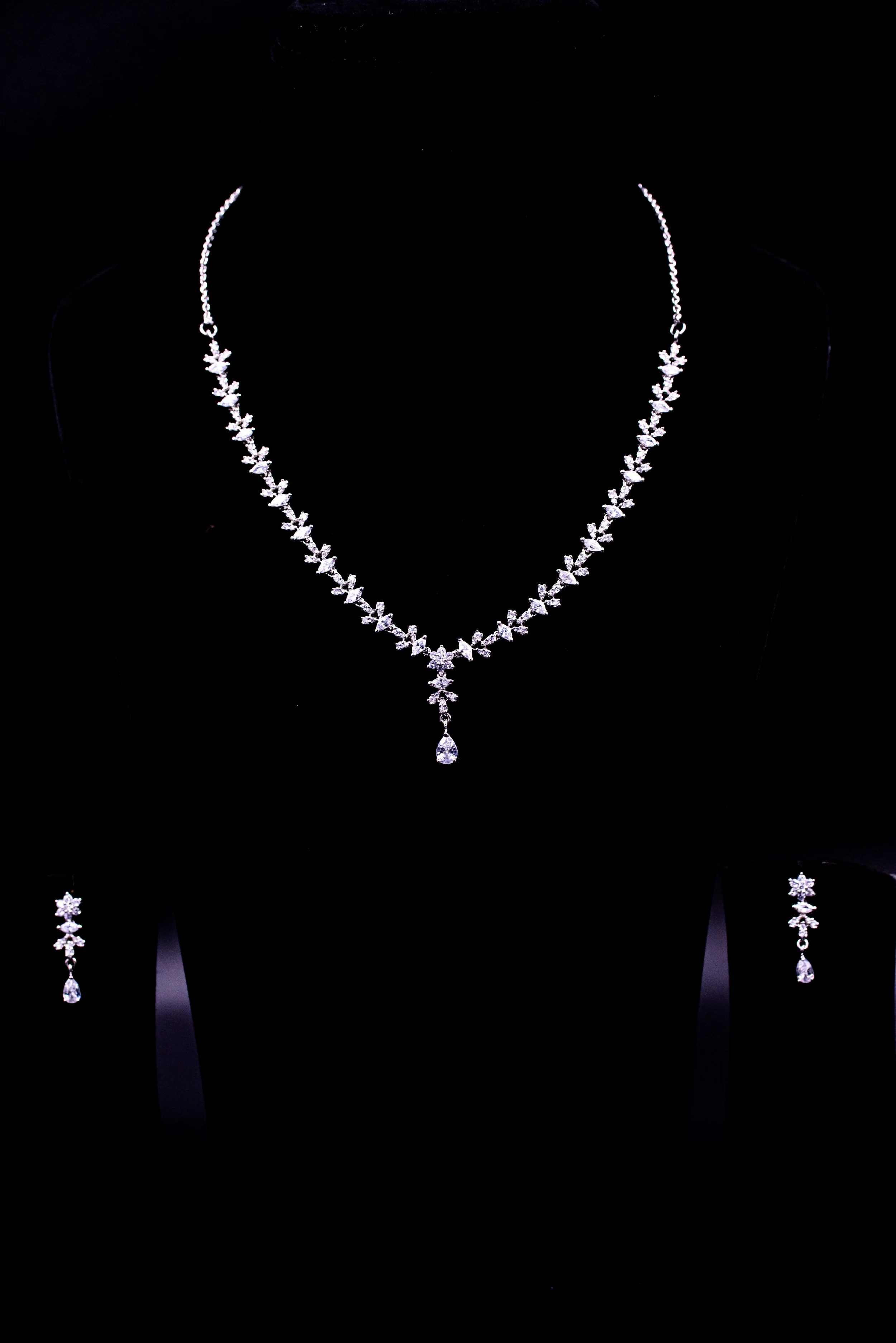 Jewelry set including a necklace and matching earrings with leaf-shaped design and teardrop-shaped pendants, displayed on a black background.