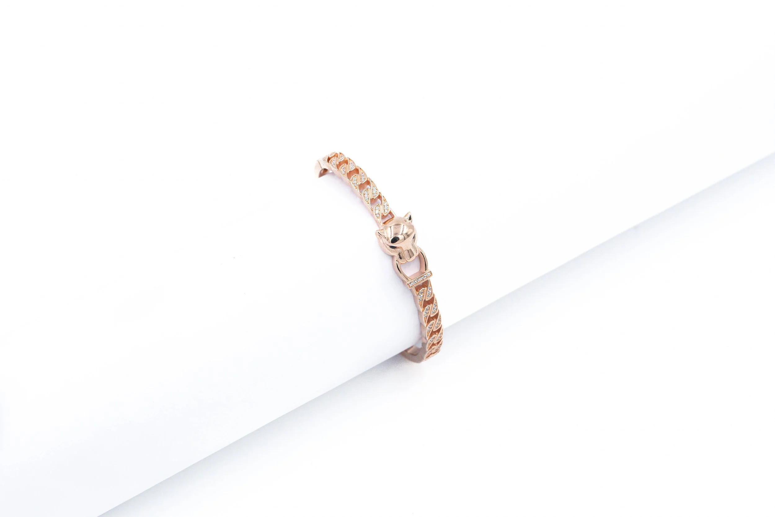 A rose gold bracelet with a skull motif and chain link design, displayed on a white cylindrical stand.