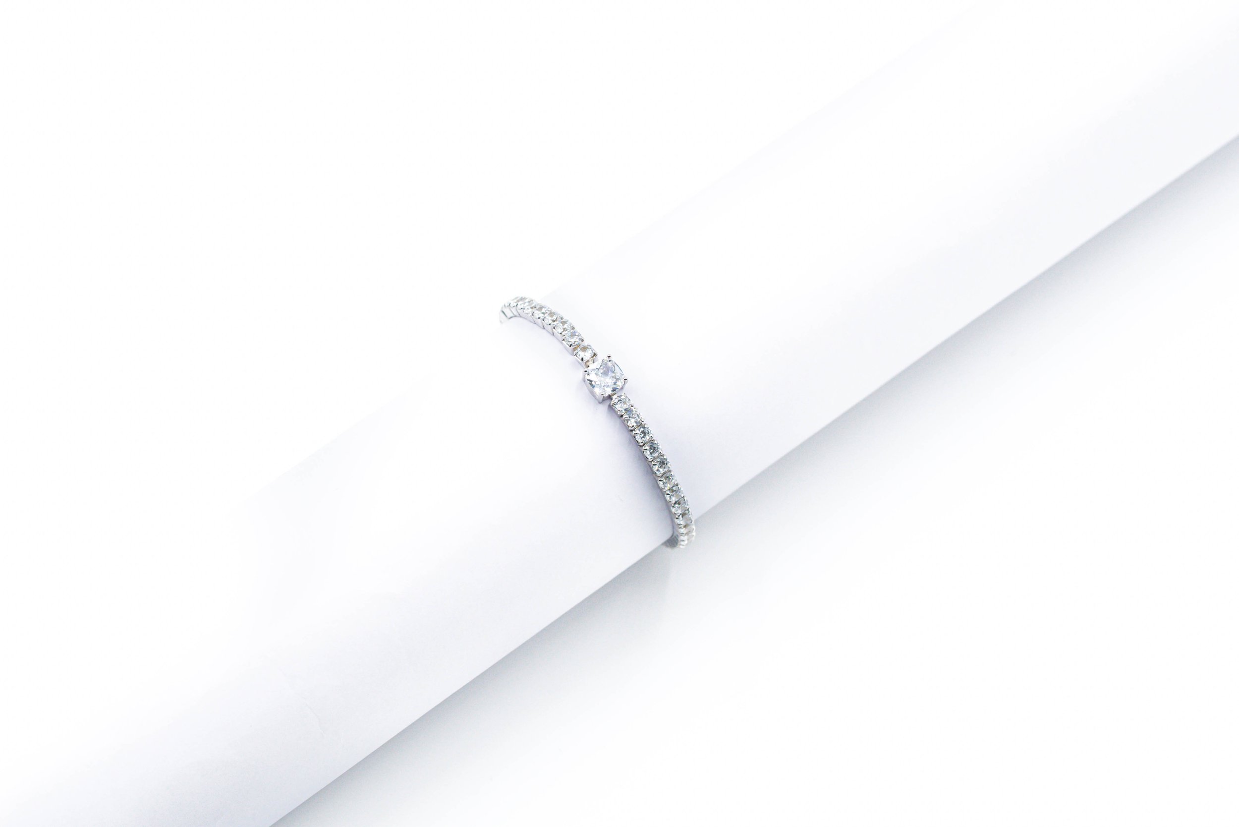 Close-up of a silver engagement ring with a central round diamond and smaller diamonds along the band, draped over a white cylindrical object.