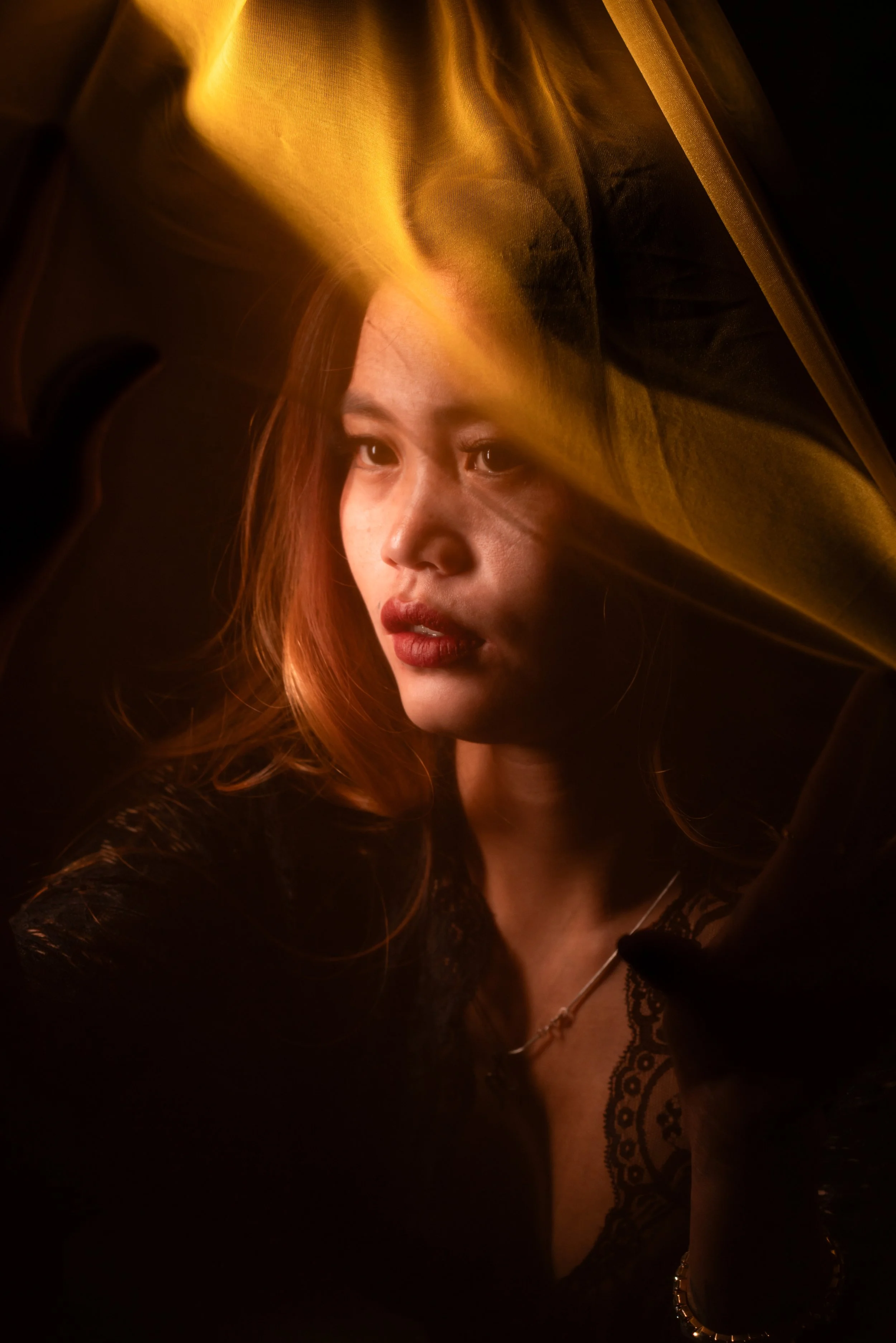 A woman with long reddish hair looking thoughtfully, with a yellow light streak across her face and a dark background.