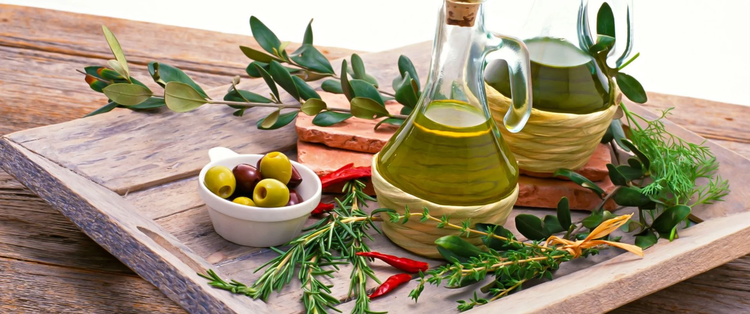 Olive oil bottles, fresh herbs, and olives on a wooden tray.