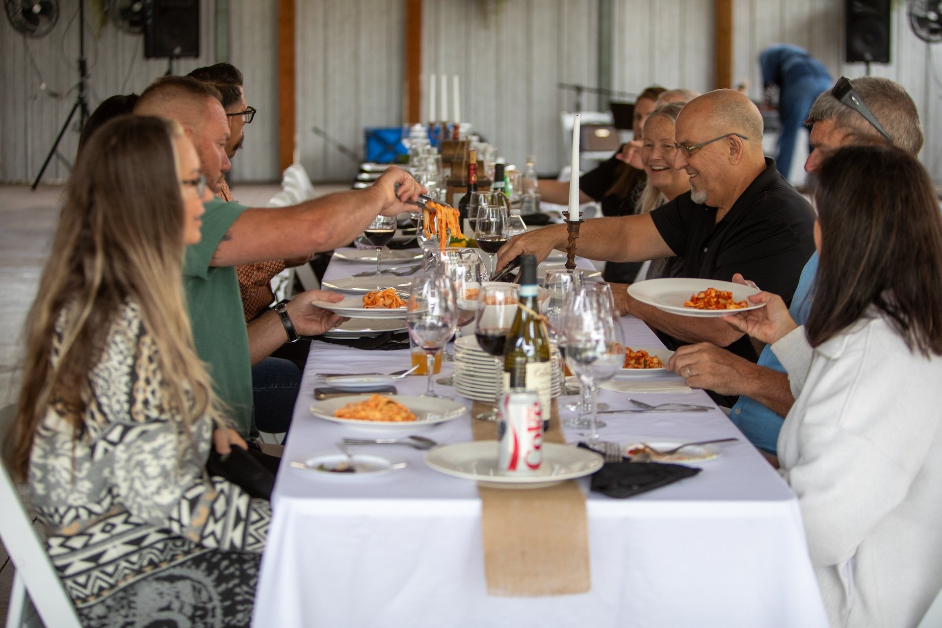 People sitting at a long dining table, enjoying a meal together in a rustic setting.