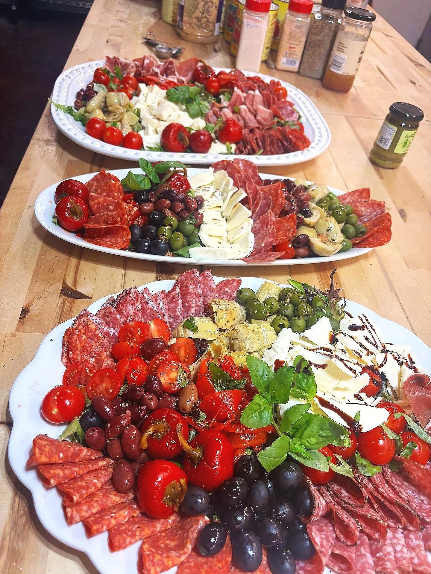 Assorted platter of cold cuts, cherry tomatoes, olives, cheese, and fresh herbs on a table.