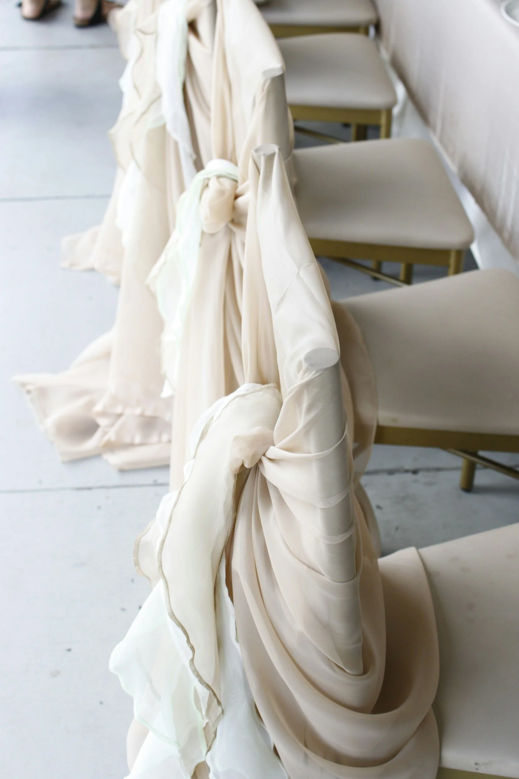Chairs draped with soft, cream-colored fabrics with tied bows, arranged in a neat row.