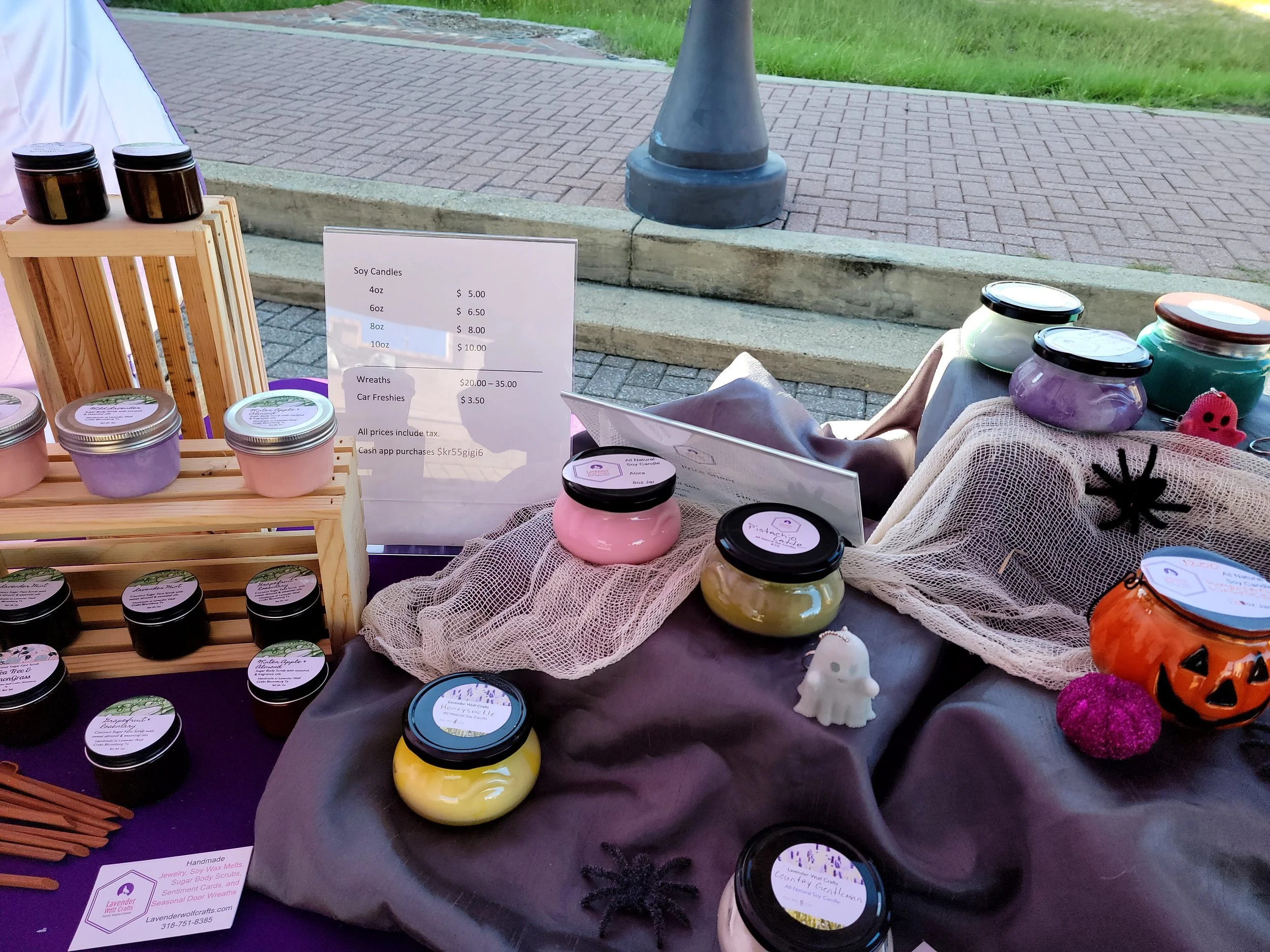 Artisan candle display at a market booth — colorful jars arranged with care on a purple cloth