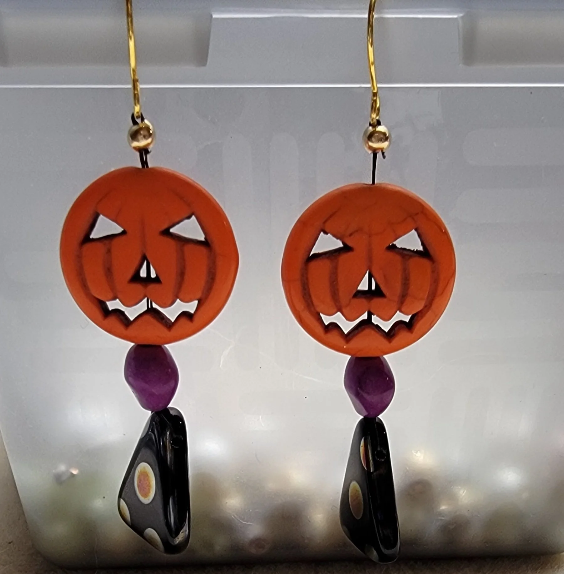 Halloween earrings with carved pumpkin faces, purple accent beads, and black teardrop charms with colorful dots