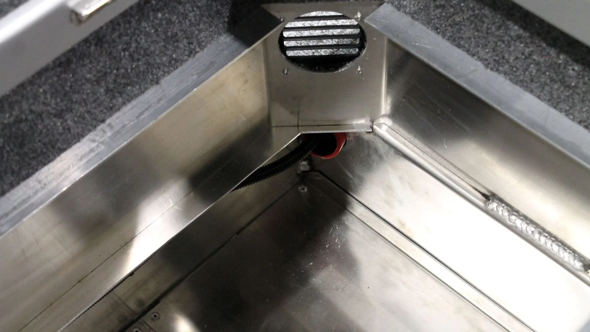 Inside view of a stainless steel machine with a circular vent and a black flexible hose connected at the bottom.